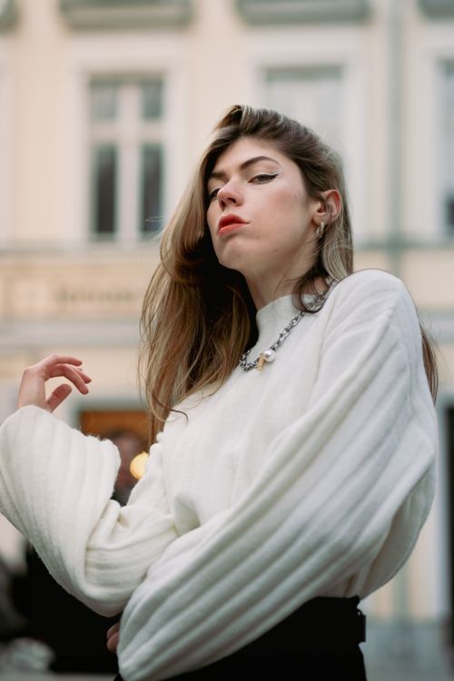 Free Stylish young woman in a white sweater posing confidently on a city street. Stock Photo