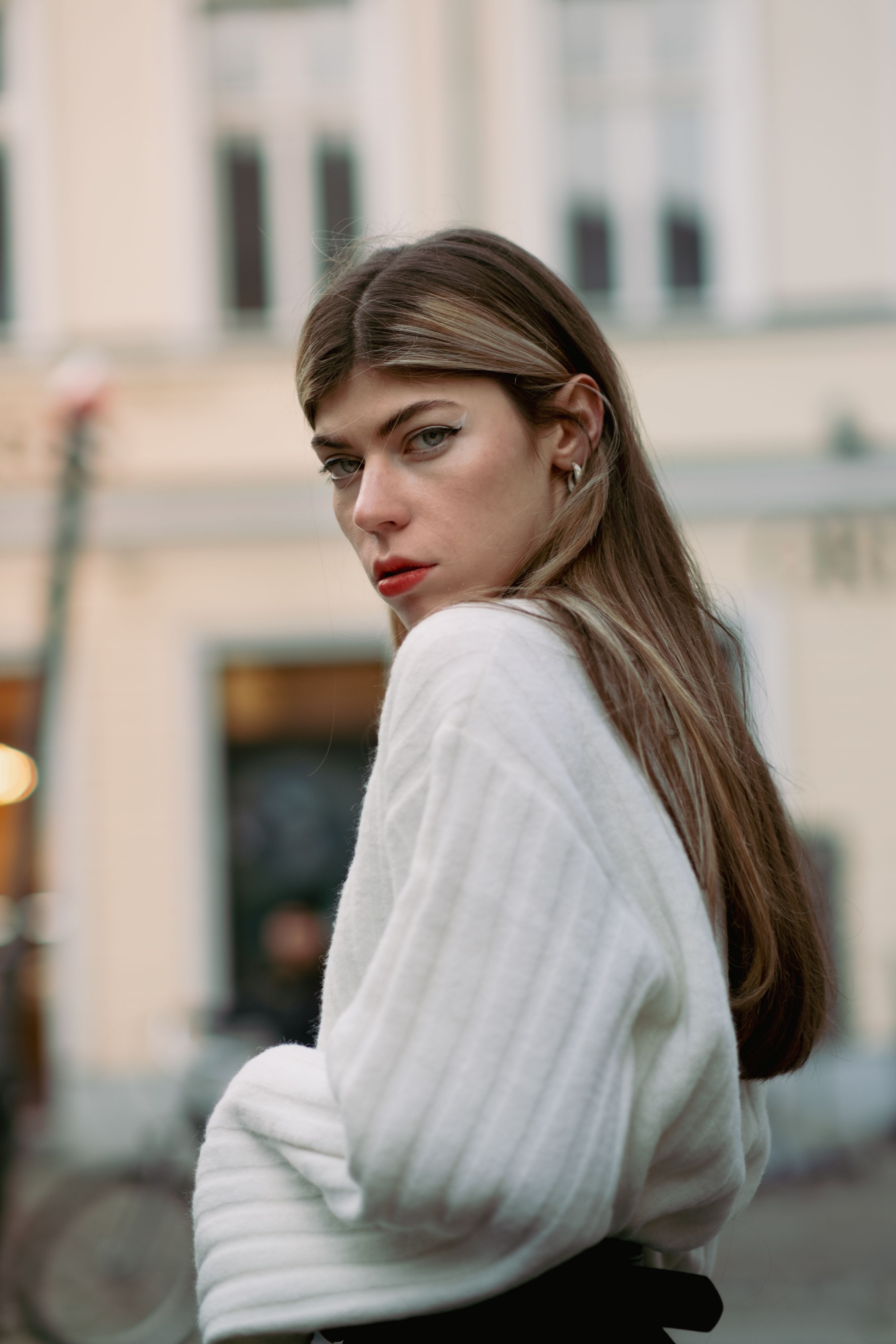 Fashionable woman in white sweater posing in a city street setting, showcasing urban style.