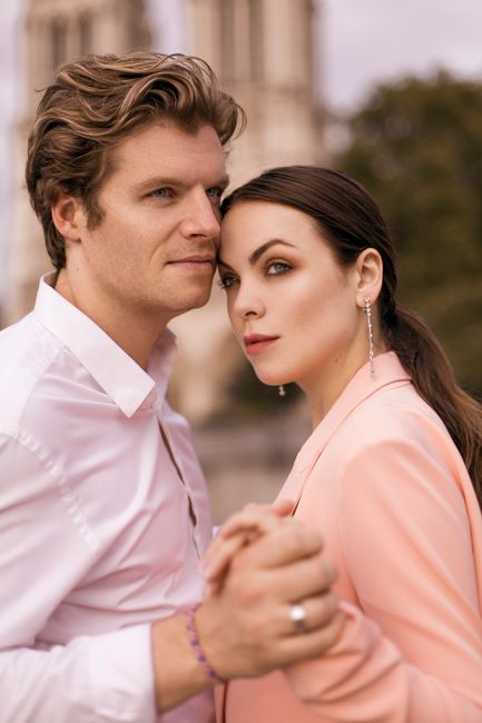 Elegant couple holding hands in an outdoor romantic setting with blurred background.