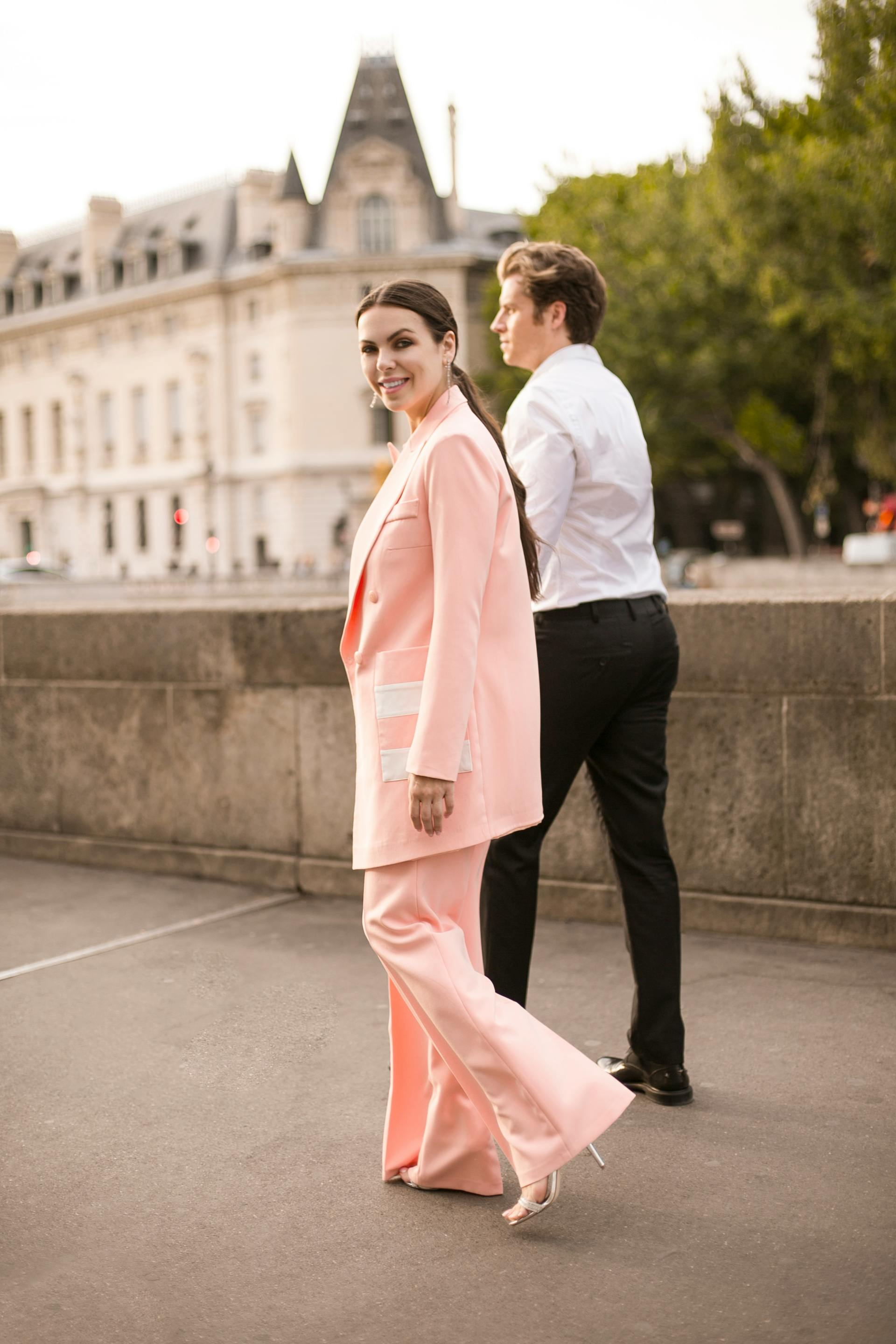 Elegant couple strolling in stylish outfits in a city setting with classic architecture.