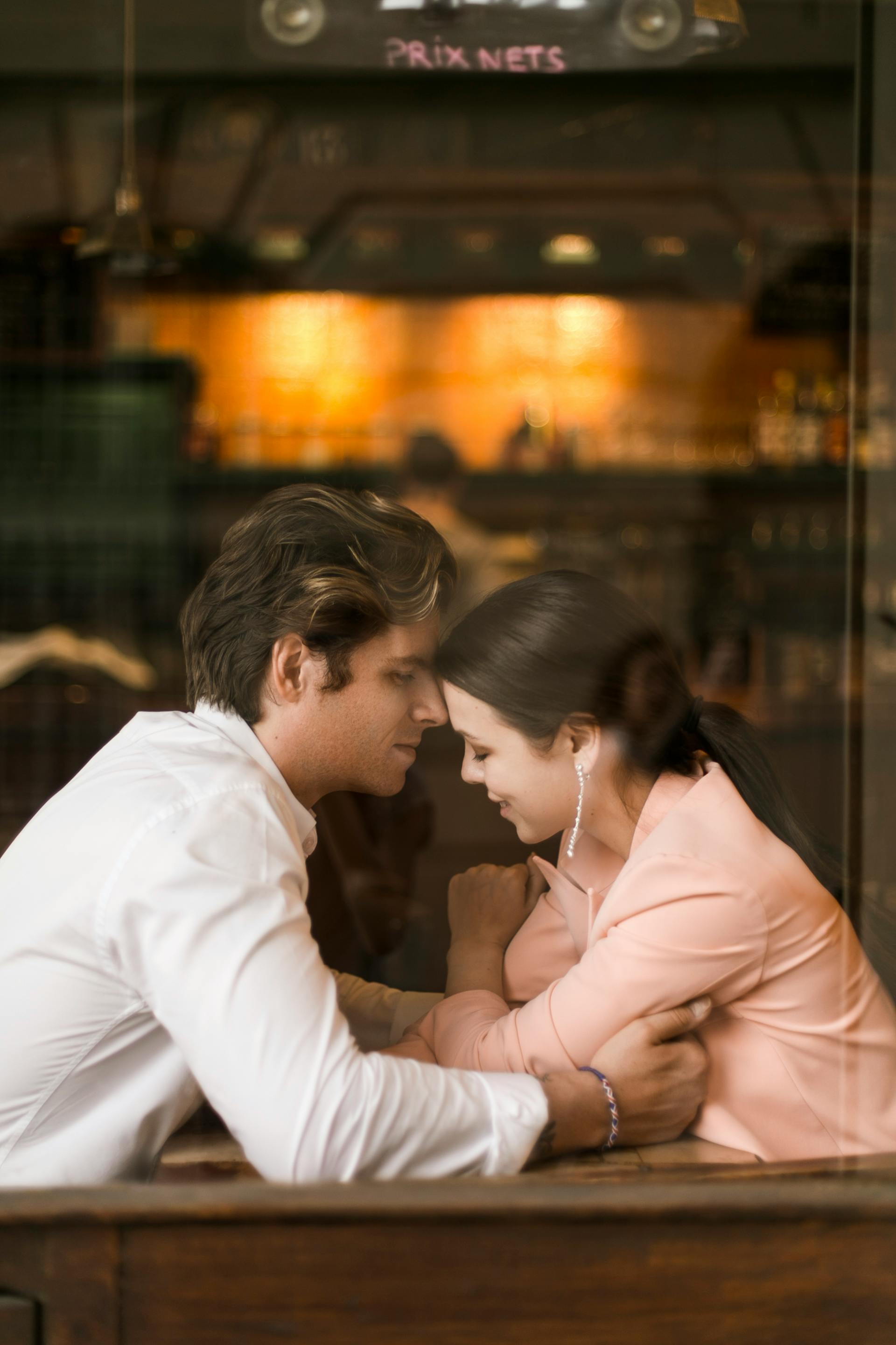 Intimate moment of couple embracing across a table in a warm, cozy restaurant setting.