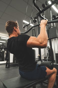An adult male performing a strength workout on a gym machine from a back view.