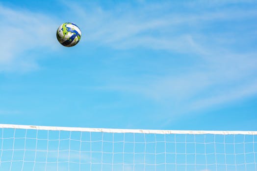 A vibrant volleyball against a clear blue sky over a net, capturing the essence of sports action and outdoor play.