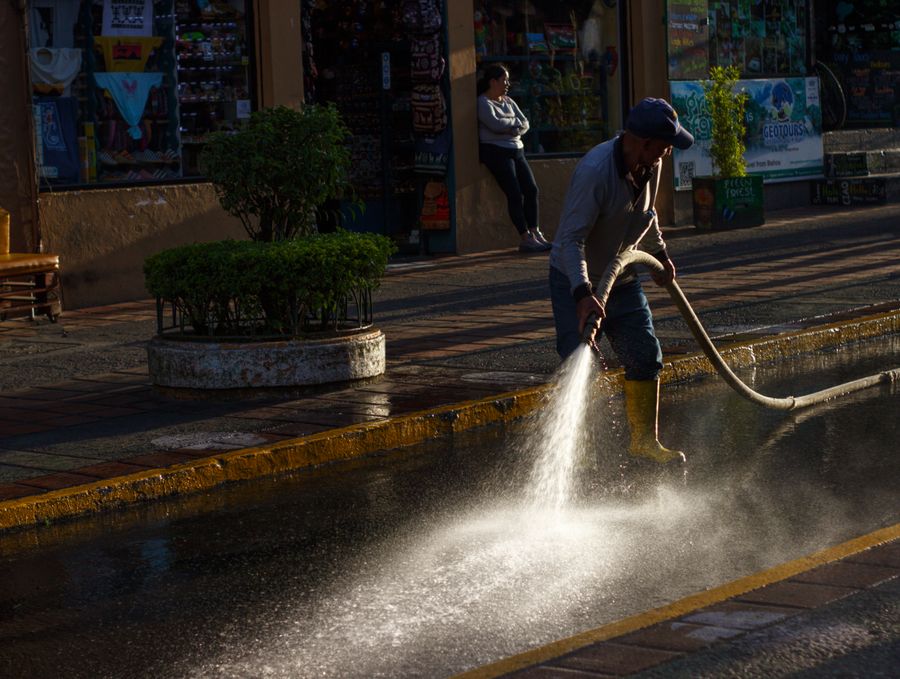 Worker rinsing a paved sidewalk in a commercial district