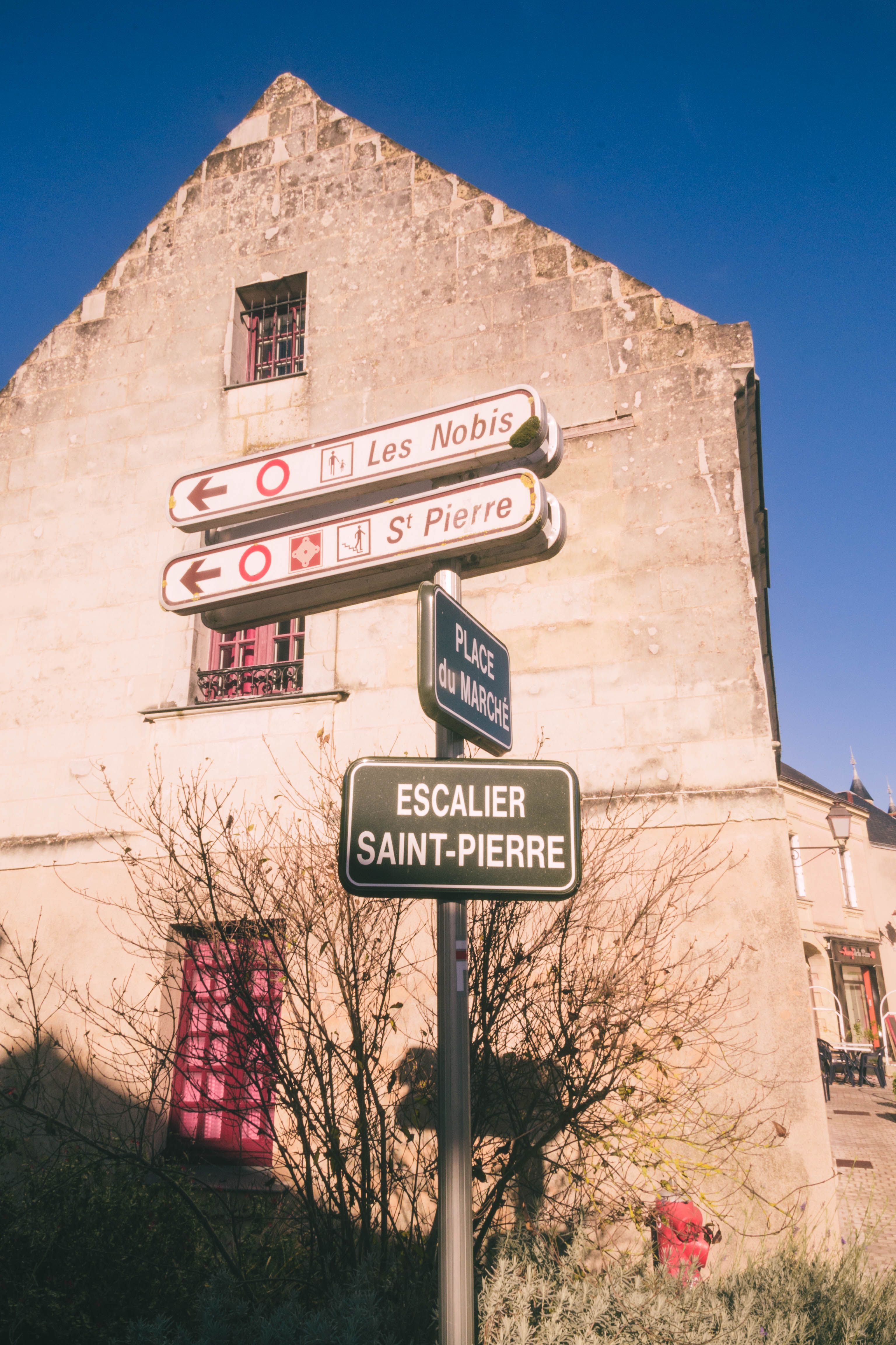 Street signs in Montreuil-Bellay with historic architecture under a clear blue sky.
