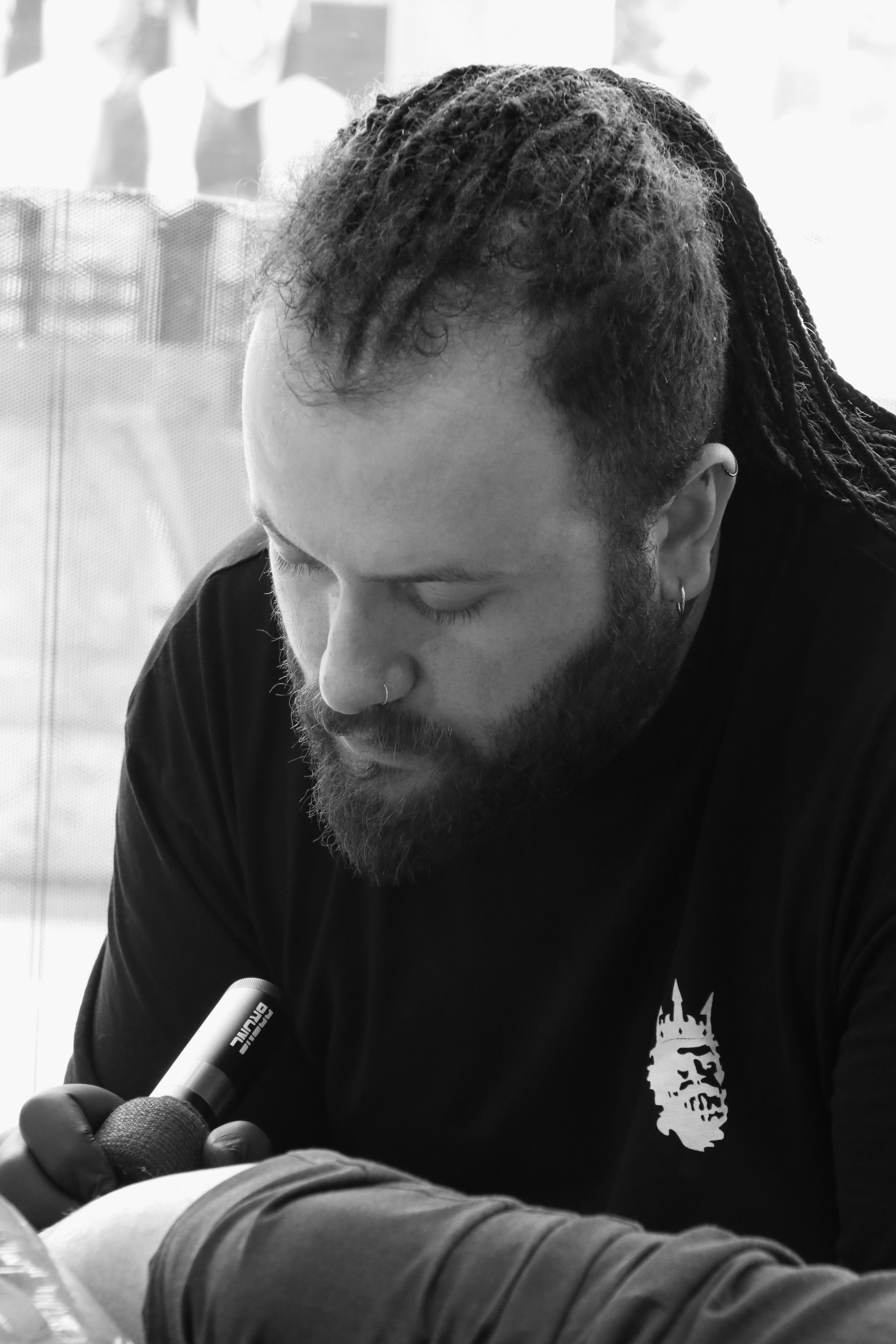 A focused tattoo artist with dreadlocks and beard working on a design in a modern studio.