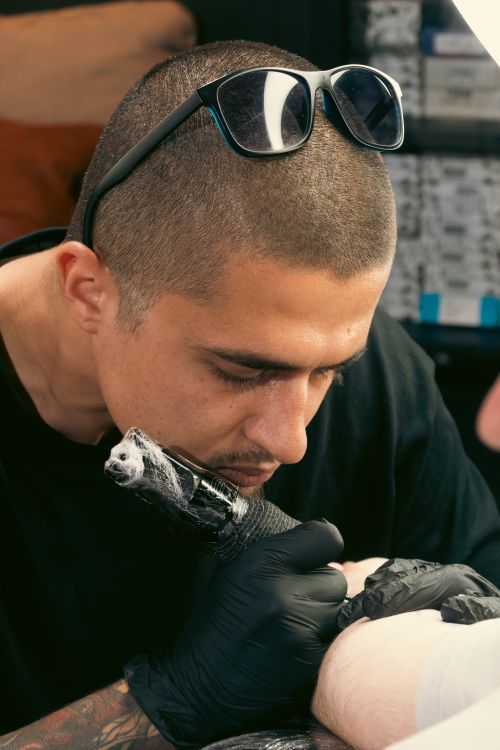 Free Skilled tattoo artist focused on tattooing a client's arm in studio setting. Stock Photo
