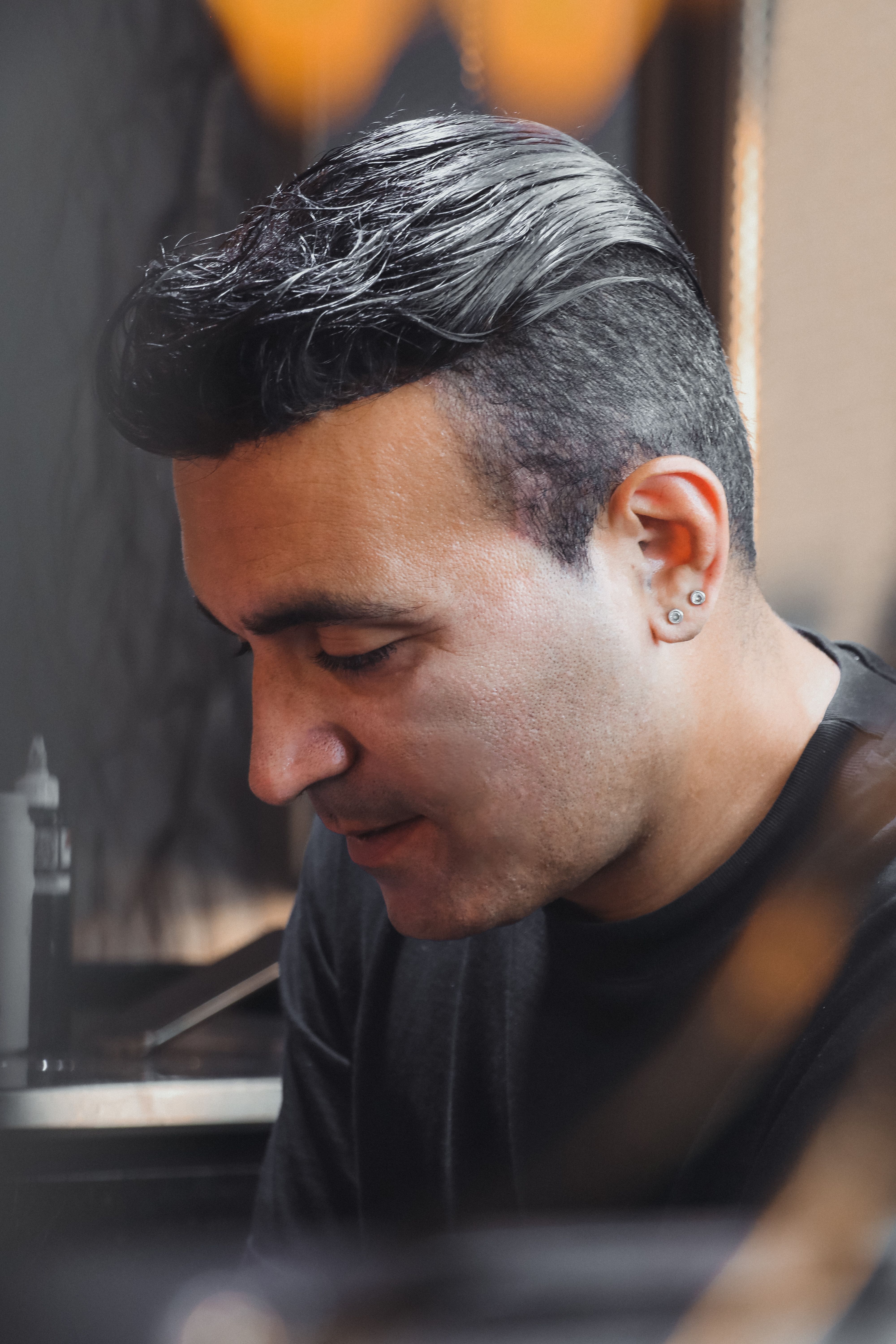 Side view portrait of a man with black hair and earrings looking down in thought.