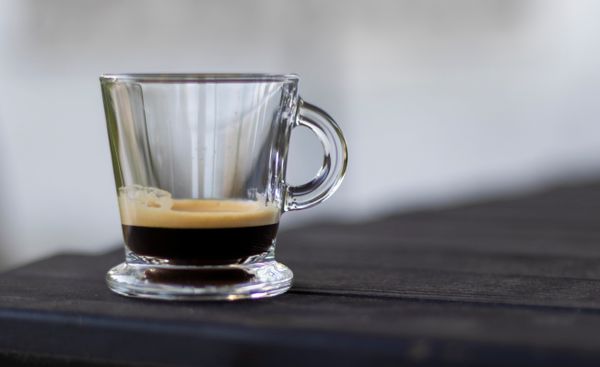 A close-up shot of a rich espresso in a clear glass cup on a dark table.