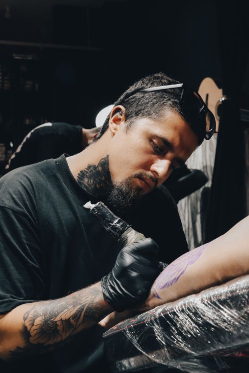 Free Close-up of a focused tattoo artist creating art on a client's arm in a dimly lit studio. Stock Photo
