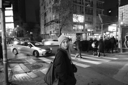 Black and white photo of a woman crossing at a city crosswalk at night.