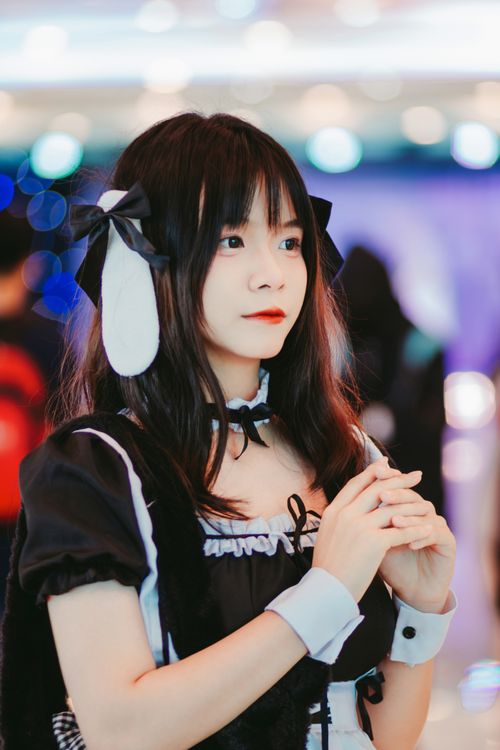 Free Elegant young woman dressed in anime-style maid costume, standing indoors with blurred lights. Stock Photo