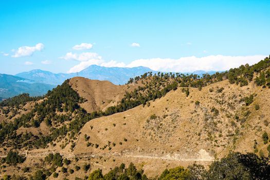 A breathtaking view of dry hills and lush trees under a bright blue sky, perfect for nature exploration.