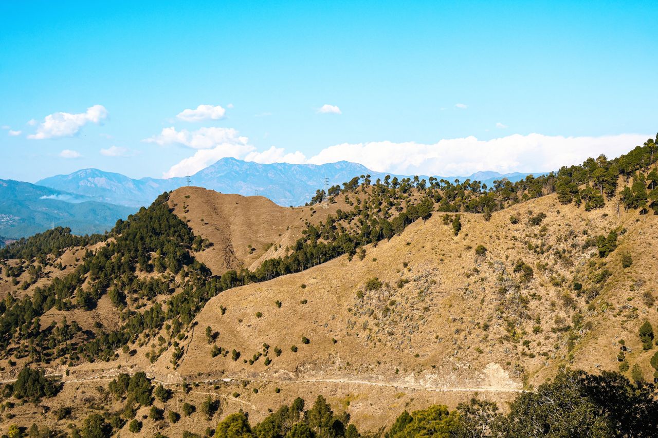 a breathtaking view of dry hills and lush trees under a bright blue sk