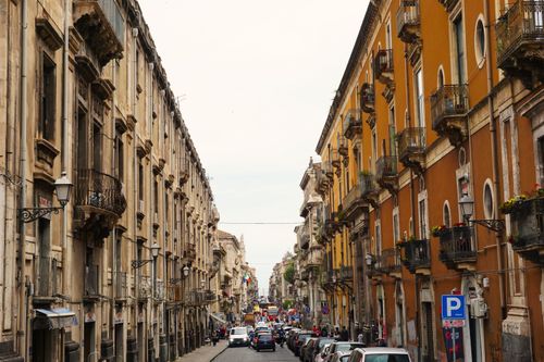 Free Charming city street with historic buildings and ornate balconies, bustling with vehicles and pedestrians. Stock Photo