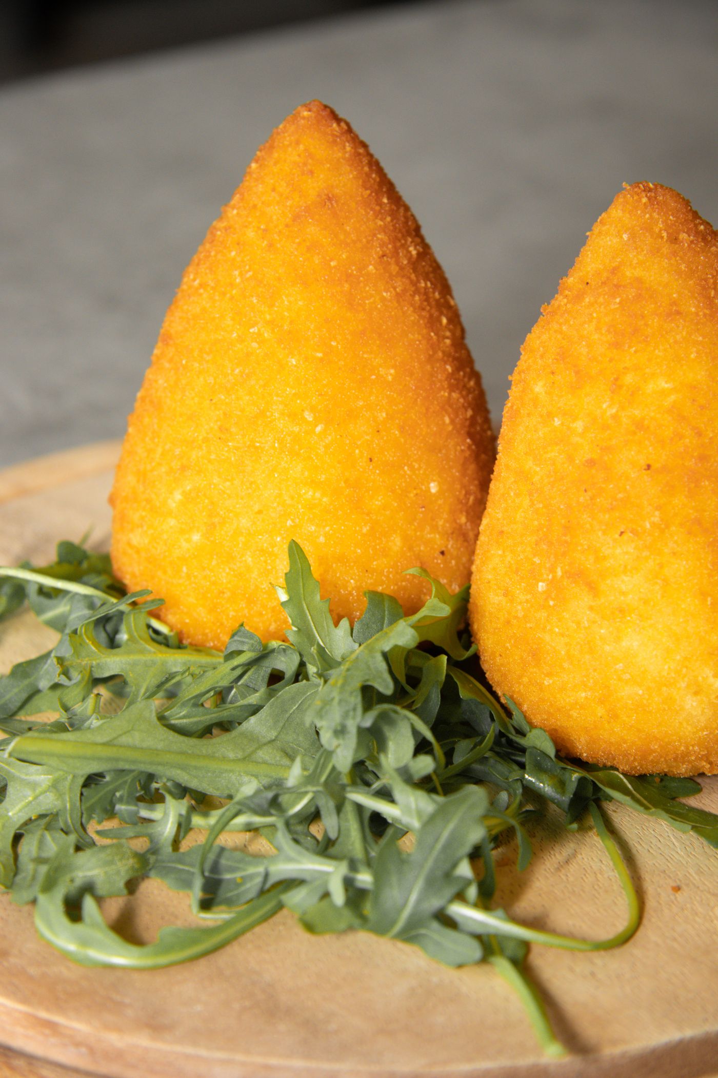 Due grandi arancine siciliane a cono, dalla crosta dorata