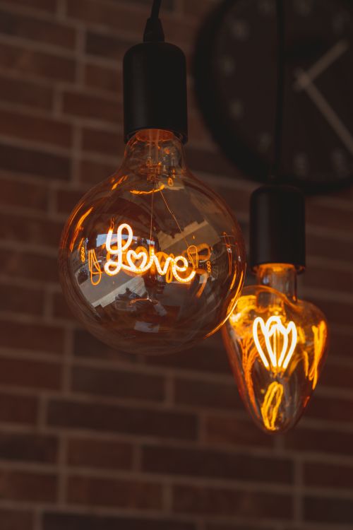 Free Warm glowing light bulbs with 'love' text against a brick wall, creating a cozy indoor atmosphere. Stock Photo