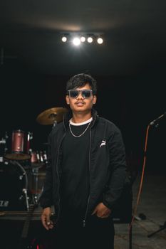 Portrait of a male musician with sunglasses standing in a music studio next to drums.