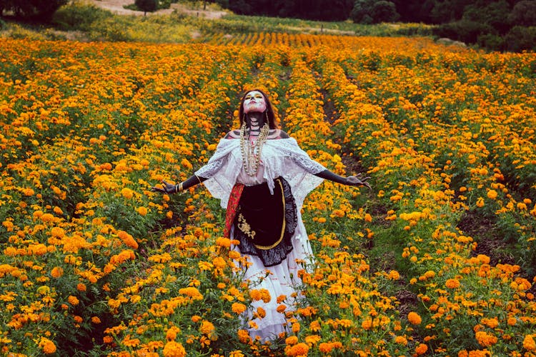 Woman Dressed As A Catrina Standing On A Field With Orange Flowers