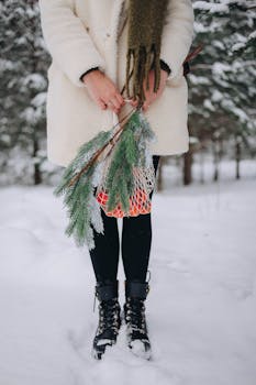 Woman in winter coat holding pine branches and tangerines outdoors in snowy forest.