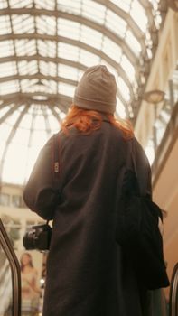Fashionably dressed woman with long red hair and hat in a mall atrium in Ankara, Türkiye.