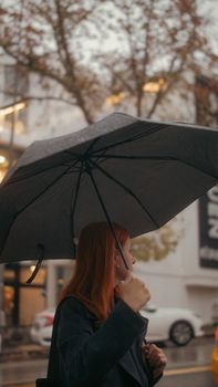 Redheaded woman holding an umbrella on a rainy street in Ankara, Türkiye.