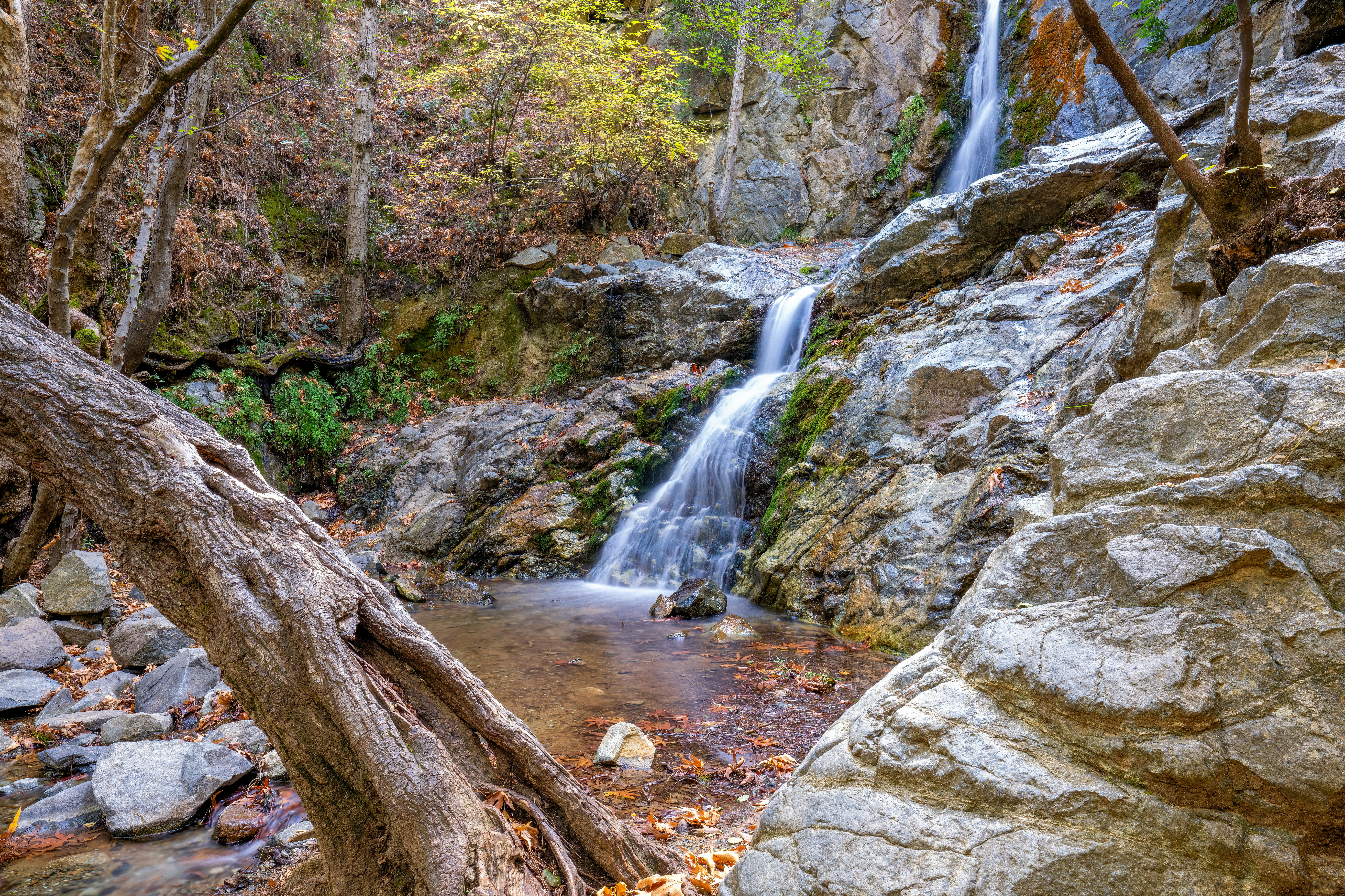 Free A tranquil waterfall cascades down rocky terrain surrounded by autumn foliage in a forest environment. Stock Photo