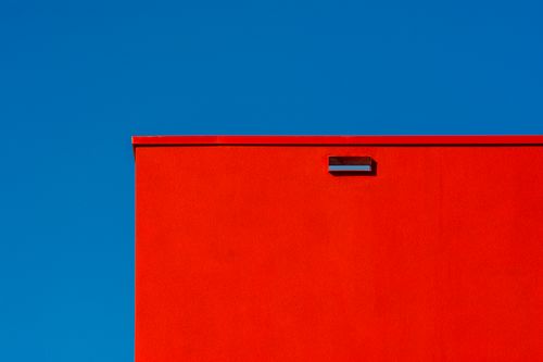 Free Minimalist image of a vibrant red wall against a bright blue sky, showcasing striking contrast. Stock Photo