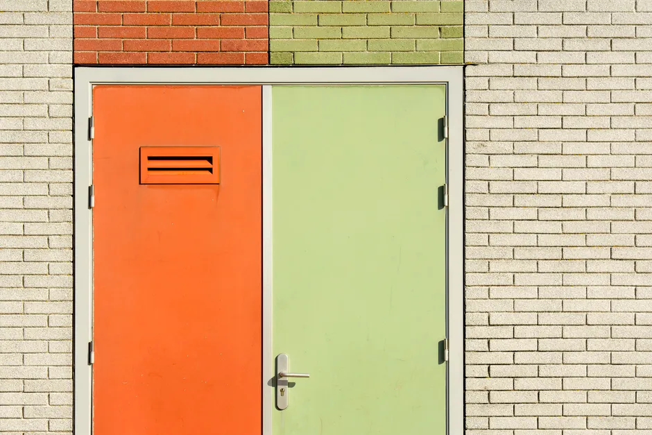 Double porte métallique orange et verte avec charnières et poignée dans mur en briques