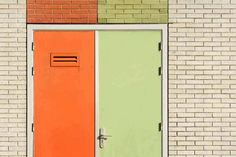 Orange and green door on a brick wall with modern design and security features.