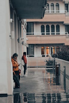 Two people in colorful jackets stand on a wet terrace, surrounded by urban architecture.