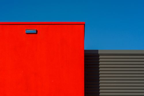 Free Striking red and gray modern facade set against a clear blue sky, showcasing architectural minimalism. Stock Photo
