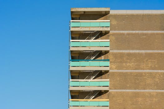 Close-up of brick apartment building facade with green balconies against blue sky.