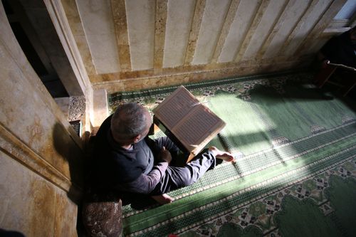Free An adult man reading the Quran inside a traditional Syrian mosque with light casting shadows. Stock Photo