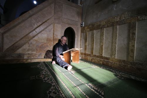 Free Middle-aged man reading at a podium inside a sunlit mosque in Idlib, Syria. Stock Photo