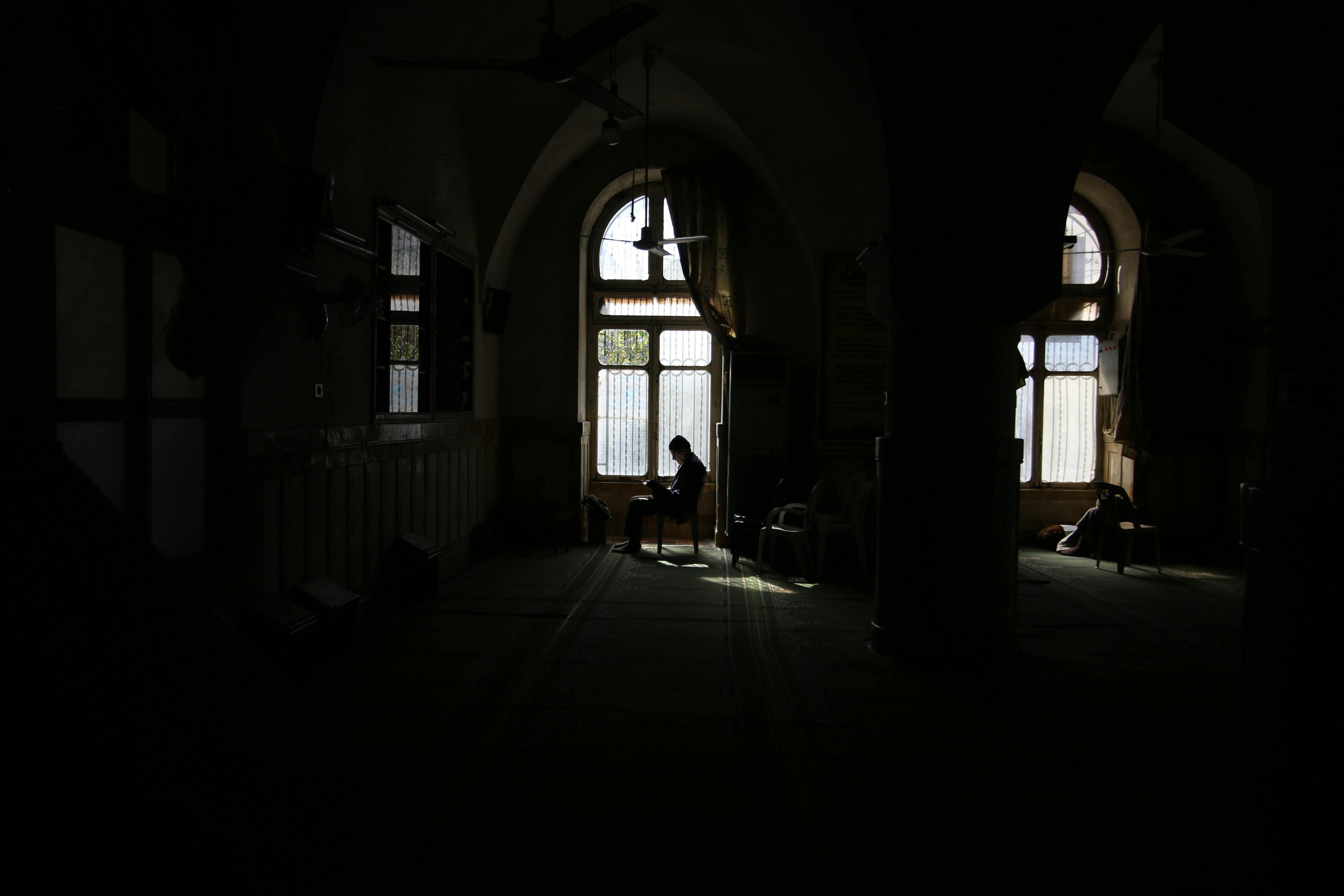 A serene silhouette of a person praying inside a mosque in Idlib, Syria, highlighting Islamic architecture.
