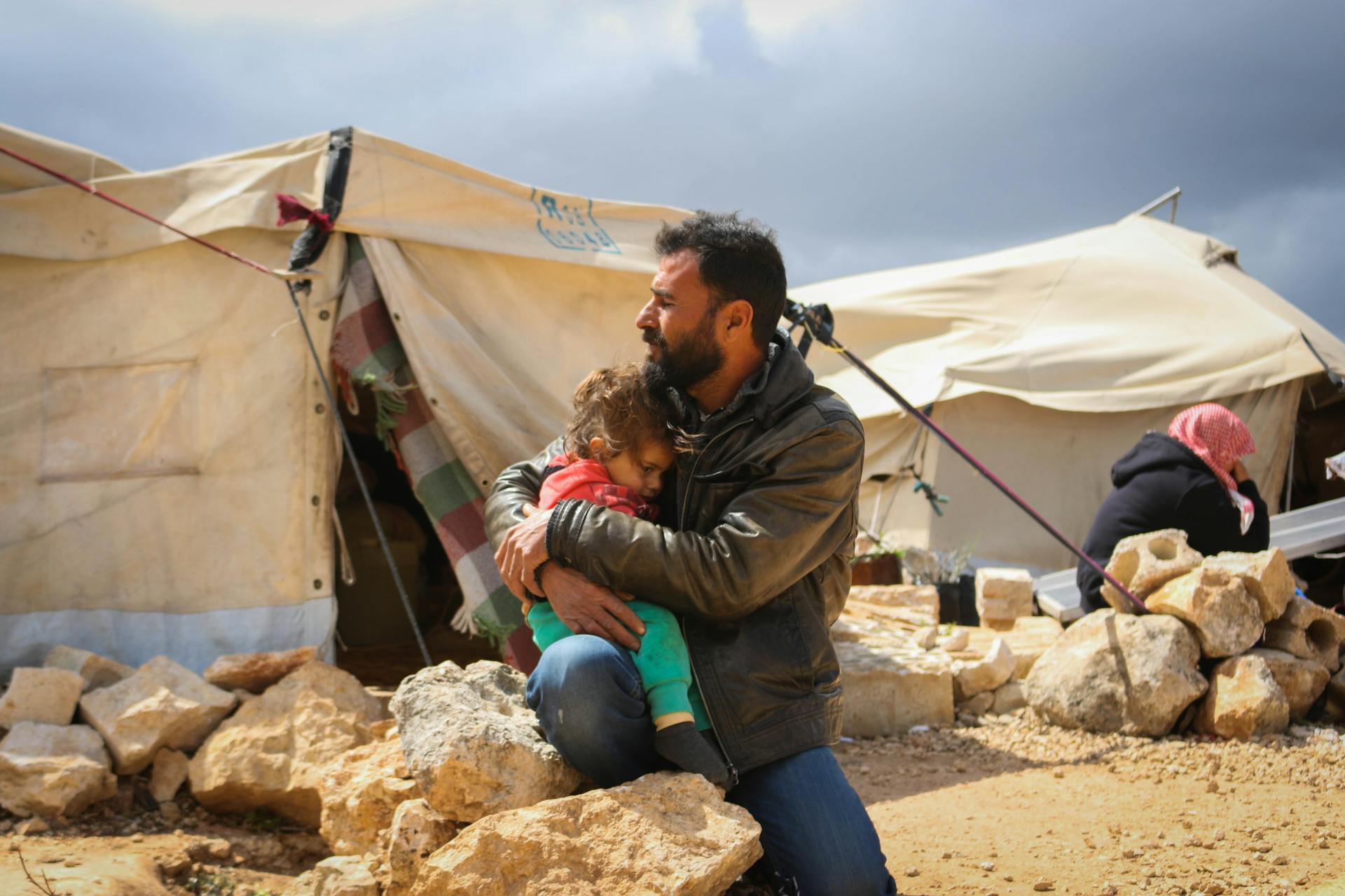 A father embraces his child outside a tent in a Syrian refugee camp.