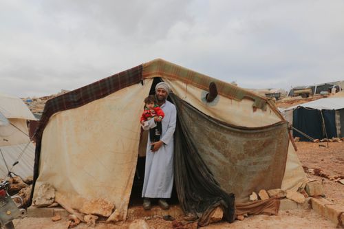 Free A father and child smiling outside their shelter in a refugee camp in Idlib, Syria. Stock Photo