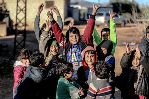 Free A group of joyful children smiling and raising their arms outdoors in Idlib, Syria, embodying happiness and playfulness. Stock Photo