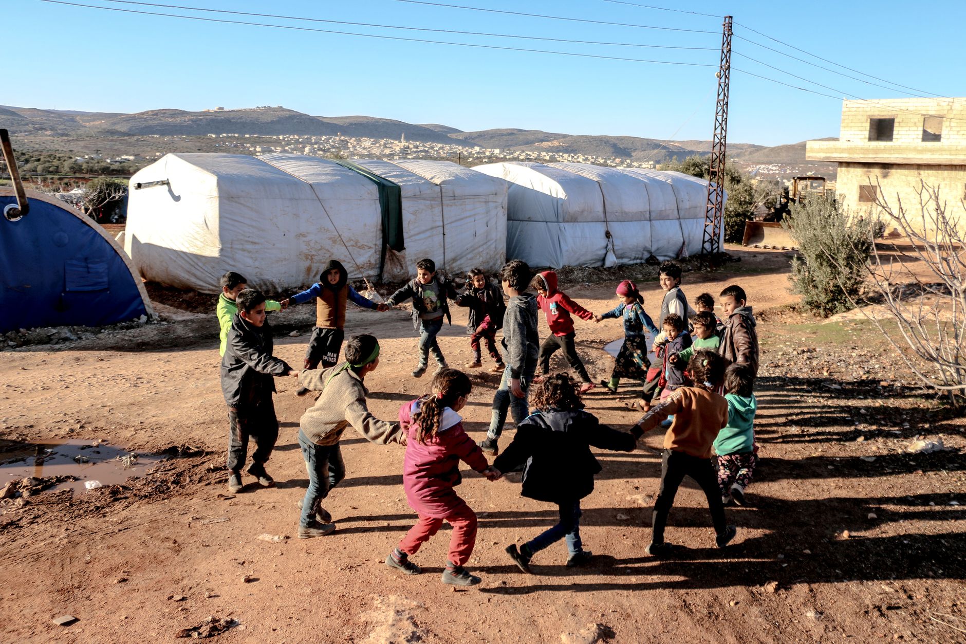 Group of children joyfully playing in a circular formation at a refugee camp in Syria.