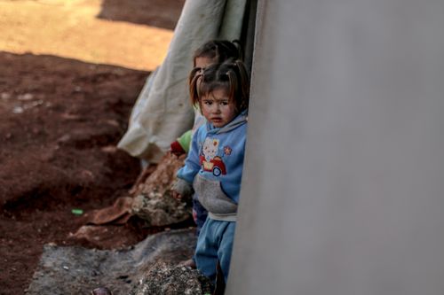 Free Children stand near a tent in a refugee camp in Idlib, Syria, reflecting resilience and hardship. Stock Photo