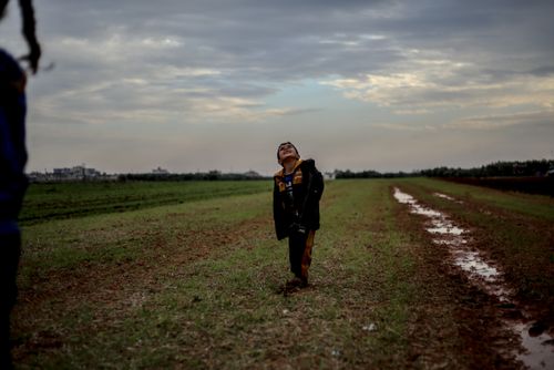 Free A young boy looks up joyfully in a muddy field near Idlib, Syria under a cloudy sky. Stock Photo