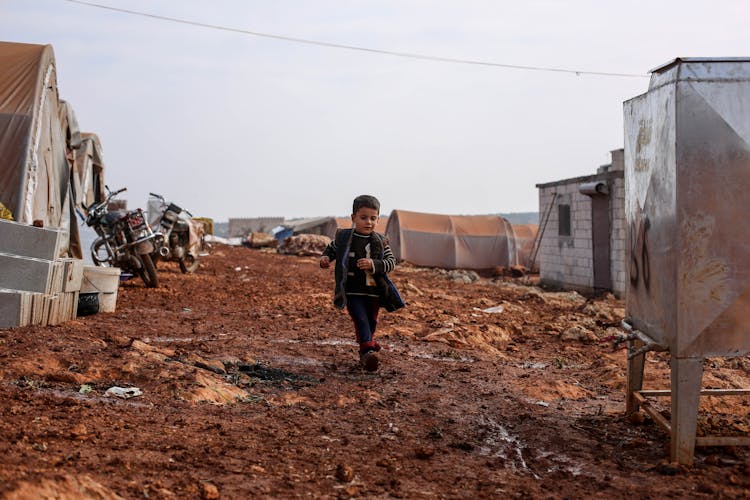 A Boy Running In The Mud At A Refugee Campsite 