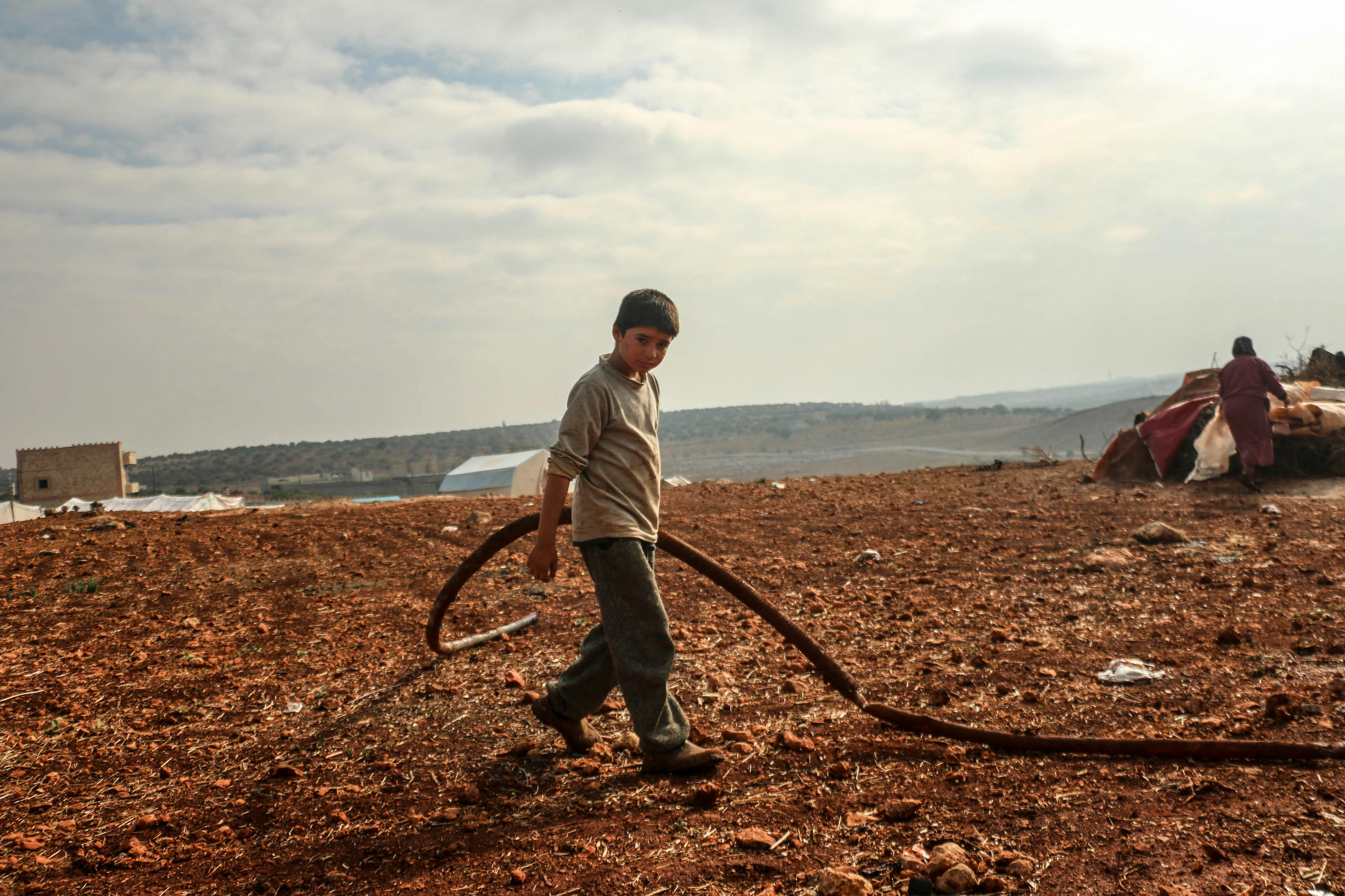 A young boy in Idlib, Syria, holds a hose in a rural field, capturing the essence of rural life.