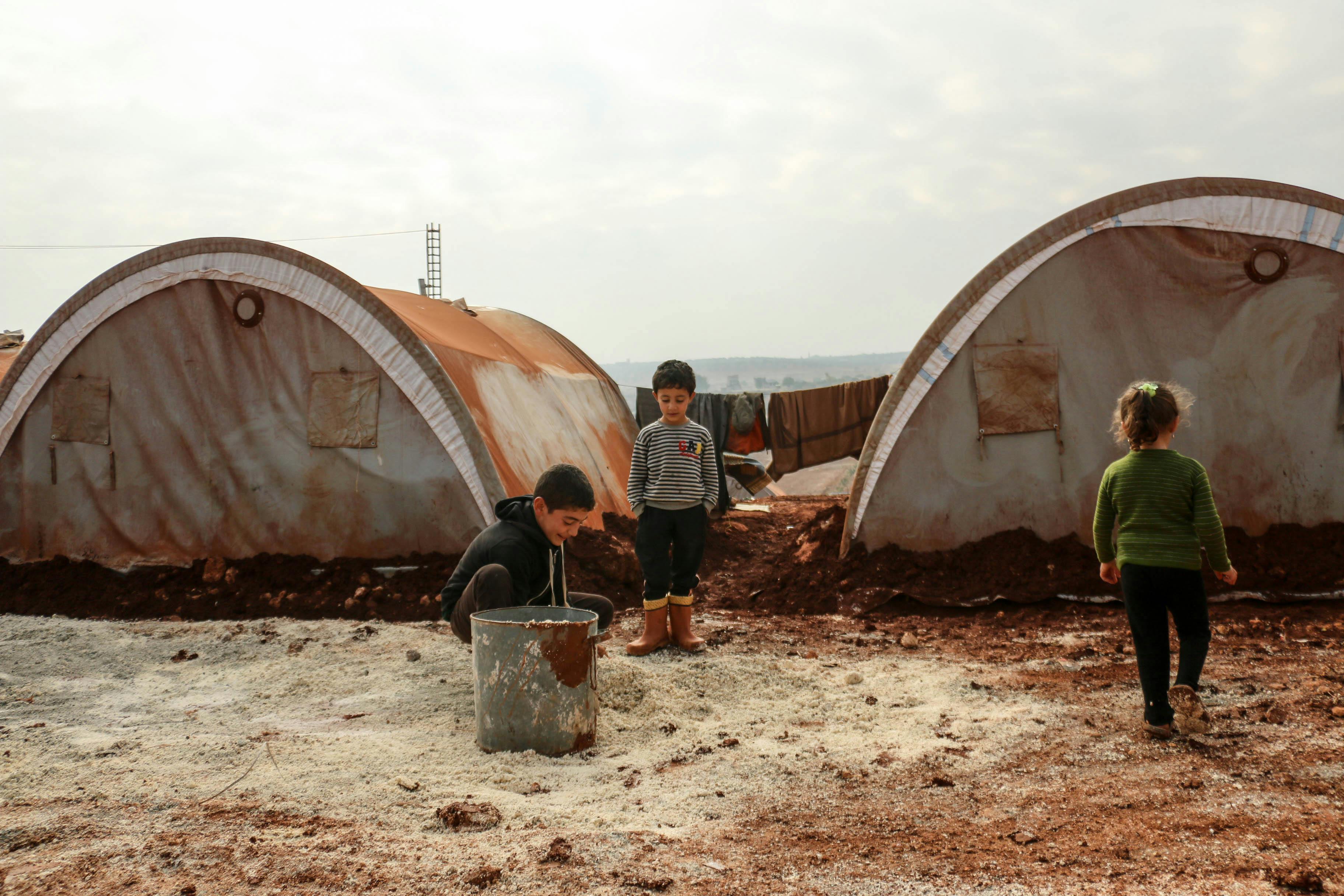 Children engaging in play near refugee tents in Idlib, Syria, amid challenging conditions.