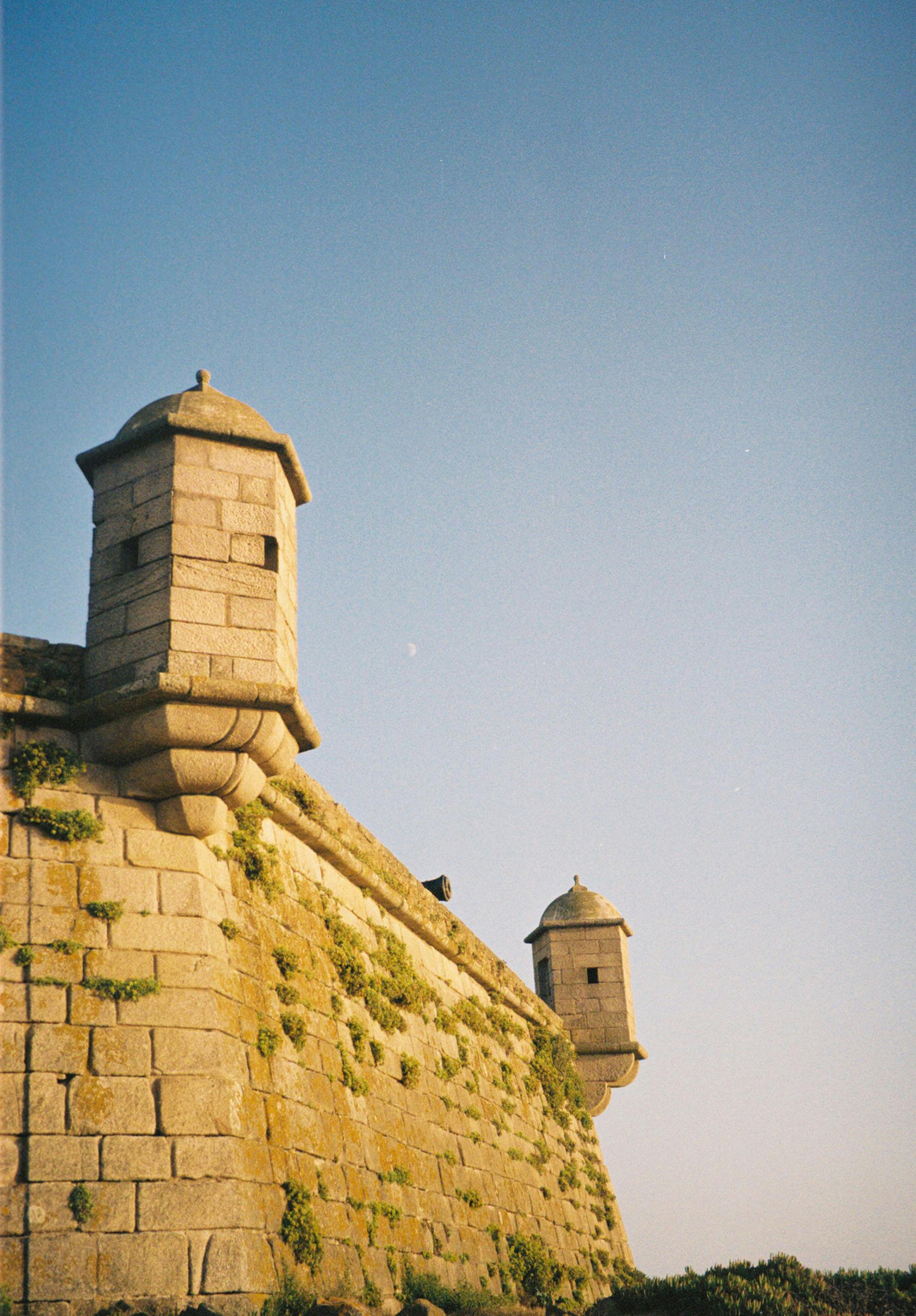 Stone watchtowers of Queijo Castle in Porto, Portugal during sunset.