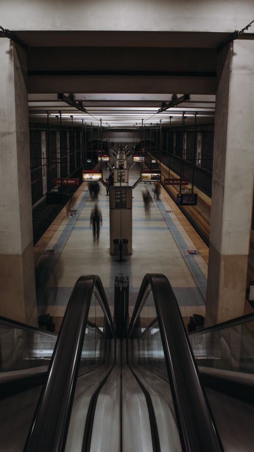 Free Dimly lit modern subway station with escalators and blurred commuters, creating a dynamic urban scene. Stock Photo