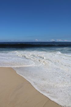 Tranquil beach in Rio de Janeiro with gentle waves and clear blue sky.