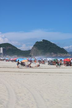 Crowded Copacabana Beach in Rio with sunbathers and distant hills under a clear sky.