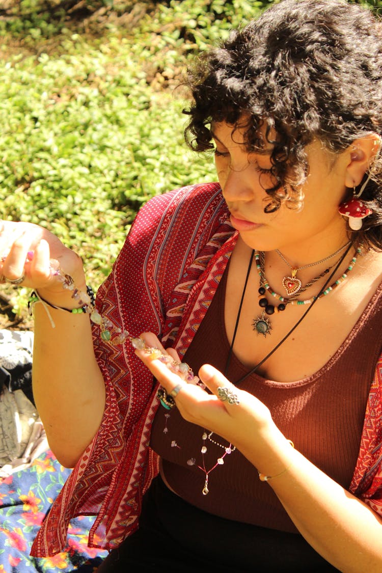 Young Woman Sitting Outside And Holding A Colorful Necklace